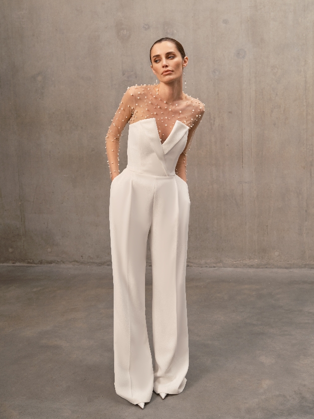 a tuxedo-inspired jumpsuit, crafted from exclusively designed crepe with a deep V-neckline featuring a structured lapel over the bust, a corseted bodice, wide-leg and long-length tailored trousers with leg pleats, silhouette-enhancing seam detailing, and functional besom pockets.